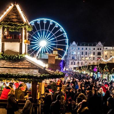 people at a Christmas market with big wheel and stalls 