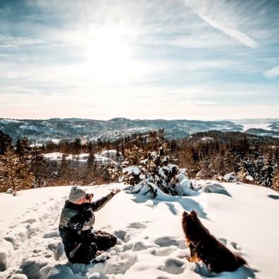 Man sitting near a dog Holding a Camera While Taking Picture of the Landscape